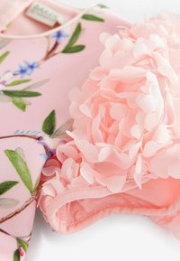 Różowa sukienka w kwiatowy wzór z zielonymi liśćmi, z teksturowanymi różowymi kwiatami na jednym ramieniu. Miękki, gładki materiał.