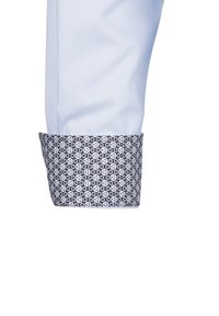 Polsino di camicia azzurra chiara con un tessuto blu scuro a motivi che presenta disegni circolari bianchi. Materiale cotone, texture liscia.