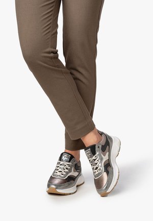 Metaalgrijze en zwarte sportschoenen met een gestructureerd mesh en gladde leren accenten. Witte, gewatteerde zool. Bruine, aansluitende broek.