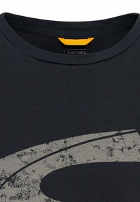 Mørkeblå bomulds t-shirt med rund halsudskæring og et struktureret grå logo foran. Har et gult accentmærke indeni kraven.