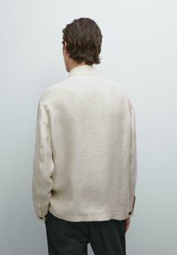 Camicia di lino beige con una vestibilità rilassata, maniche lunghe e un colletto piccolo. Presenta una superficie testurizzata e polsini con bottoni.