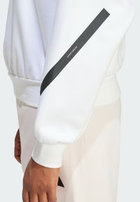 Biely sveter s textúrovaným povrchom, s čiernym diagonálnym pruhom a textom "SPORTSWEAR" na rukáve, s rebrovanými manžetami a lemovaním.