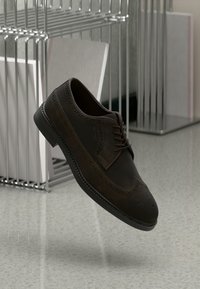 Tamnosmeđi suede brogue cipele s uzdignutim detaljima i vezicama, s crnom gumiranom potplatom i klasičnim vtip dizajnom.
