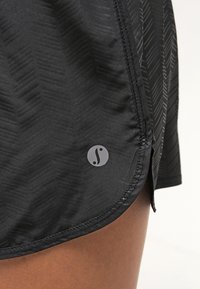 Czarne sportowe spodenki z teksturowanym wzorem jodełki, bocznym rozcięciem i naszywką z logo na dole. Gładka tkanina o subtelnym połysku.