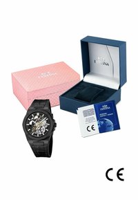 Schwarze Festina Skelettuhr mit Lederarmband, rosa und blauen Markenboxen sowie einem internationalen Garantiebuch mit CE-Kennzeichnung.