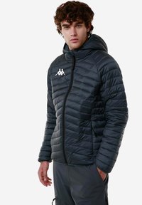 Giacca nera imbottita con zip frontale, cappuccio e logo. Presenta una texture trapuntata e due tasche laterali con polsini elastici.
