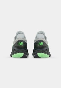 Et par sorte og grå New Balance sneakers med neongrønne sprøjt og logo, set fra bagsiden, på en hvid baggrund.