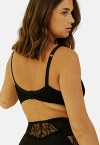 Soutien-gorge noir avec bretelles réglables, un design sans couture et une fermeture à crochets. Des détails en dentelle ornent le dos pour un toucher texturé supplémentaire.