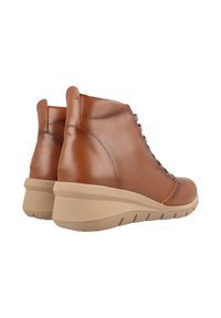 Botas de cuero marrón hasta el tobillo con punta redondeada, cordones en la parte delantera y una suela de cuña en tono beige claro con detalles texturizados.