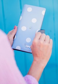 Light blue wallet with white polka dots, snap closure, and silver charm. Smooth texture with contrasting gray interior visible.