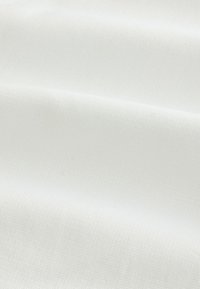 Tissu blanc avec un fin motif quadrillé texturé et de douces plis créant des ombres légères.