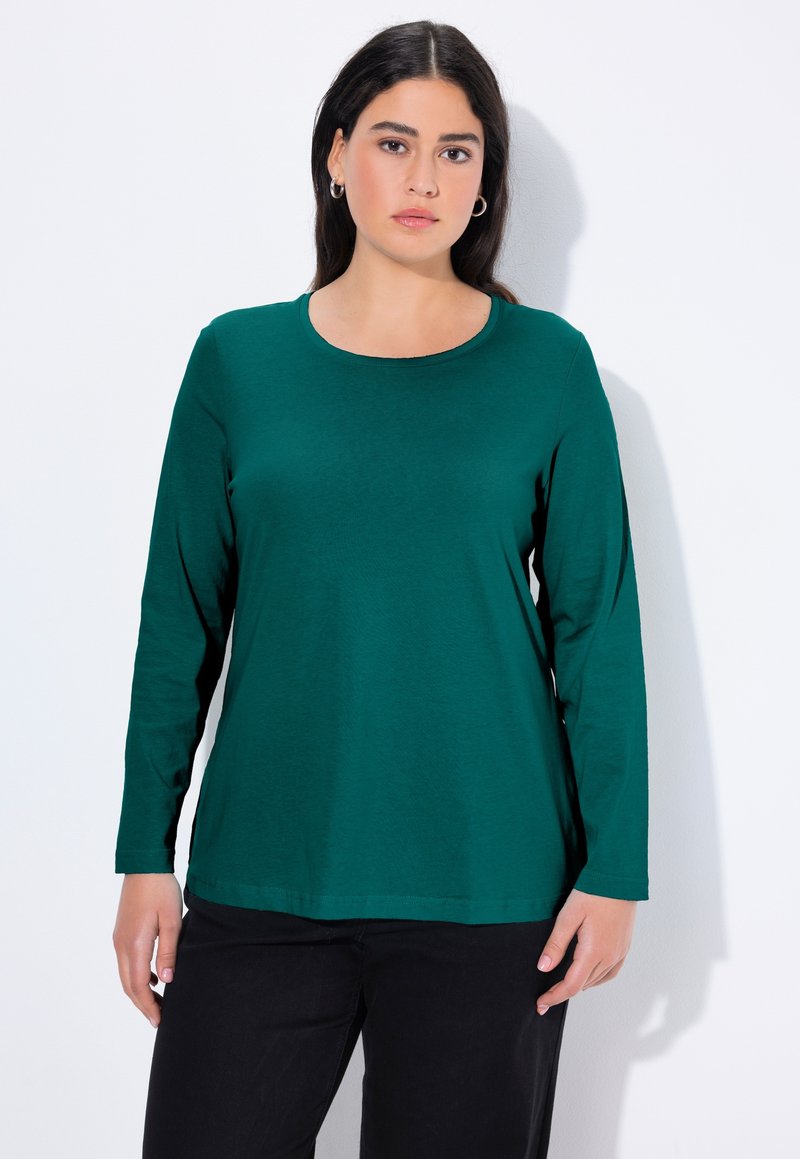 Zielona bluzka z długim rękawem, wykonana z miękkiego materiału, z okrągłym dekoltem, o luźnym kroju i gładkiej fakturze. W połączeniu z czarnymi spodniami.