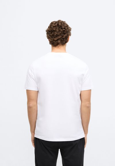 Balta kokvilnas T-krekls ar apaļu kaklu un īsām piedurknēm, redzams no aizmugures. Gluda tekstūra, vienkāršs dizains, bez redzamiem logotipiem vai rakstiem.