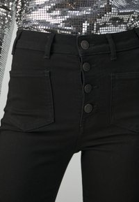 Černé džíny s vysokým pasem, které mají čtyři knoflíky vpředu, dvě zadní kapsy a hladký denimový materiál.