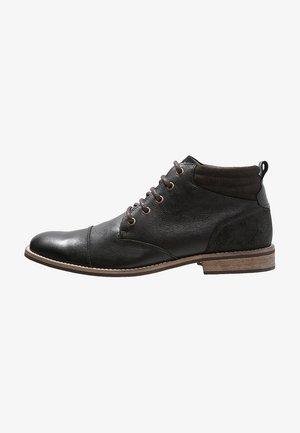 Bottine pour homme en cuir noir avec lacets marron, col rembourré, bout renforcé et petit talon en bois, présentée de profil sur fond blanc.