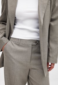 Pilkas pritaikytas švarkas ir kelnės, pagamintos iš tekstūruotos medžiagos. Švarkas turi vieną mygtuką ir kišenes, derinamas su balta raukšlėta palaidine.