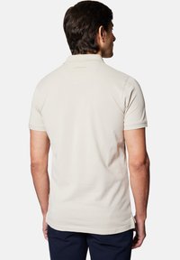 Beżowa koszulka polo z bawełny, z klasycznym kołnierzykiem, krótkimi rękawami i subtelnie umieszczonym logo marki na plecach.