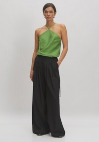 Groene satijnen camisole met dunne bandjes, gecombineerd met hoog-waist zwarte broek met wijde pijpen, met plooien en een trekkoord in de taille.