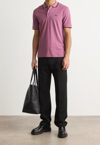 Rosa polo skjorta med svarta detaljer, svarta byxor, svarta skor och en svart toteväska. Skjortan har en tre-knapps placket och logotyp.