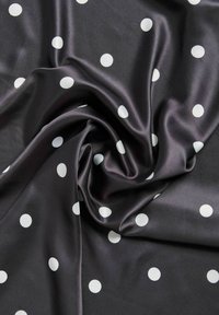 Zwarte satijnen stof met witte polka dots, die een gladde textuur en een gedrapeerd patroon vertoont, wat zachte plooien en kreukels creëert.