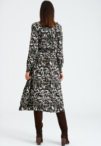 Robe longue à motifs dans des tons foncés de vert, noir et blanc avec une taille smockée et des manches longues, associée à des bottes marron en suède montantes jusqu'au genou.