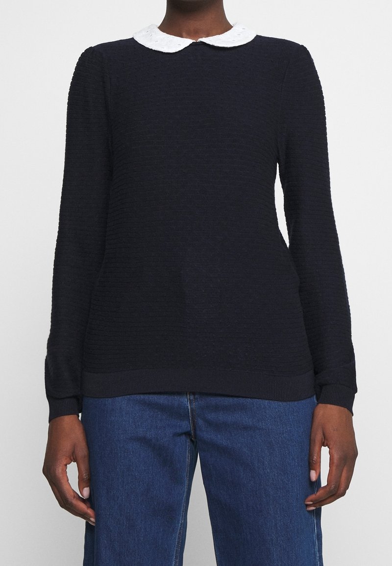 Marinblå långärmad tröja i texturerad tyg, vit Peter Pan-krage och ribbade muddar och nederkant. Matchad med blå denimbyxor.