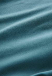 Textuurachtig teal stof met een zachte, gladde oppervlakte, die subtiele golven en variaties in licht en schaduw over het materiaal toont.