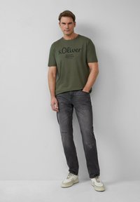 Oliwkowa koszulka z czarnym napisem, w połączeniu z wytartymi ciemnoszarymi dżinsami i off-white trampkami. Prosty design, swobodny krój.