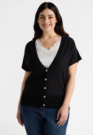 Cardigan noir à manches courtes, décolleté en V profond, et boutons dorés sur le devant. Matériau doux avec une taille côtelée. Associé à un haut blanc.