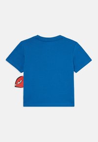 Blå bomulls t-skjorte med rund hals og korte ermer, med en grafisk detalj av røde lepper som stikker frem fra venstre side.