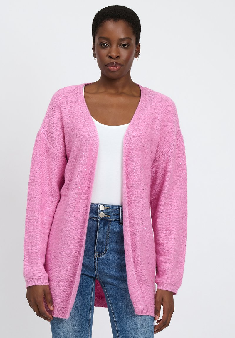 Roze gebreide cardigan met een losse pasvorm, lange mouwen en een V-hals. Heeft subtiele sprankelingen en geribbelde manchetten, gecombineerd met een witte top en denim jeans.