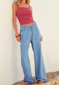 Czerwony i niebieski top na ramiączkach w paski, zestawiony z jasnoniebieskimi, szerokimi dżinsami o luźnym kroju z wiązaniem w pasie i przednimi kieszeniami.