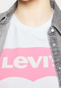 White cotton t-shirt featuring a large pink Levi's logo. Layered with a gray denim jacket, displaying visible buttons and a textured fabric.