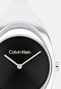 Montre Calvin Klein avec un cadran noir et des aiguilles argentées, dotée d'un boîtier en argent lisse et d'un design minimaliste.
