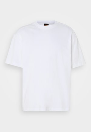 Camiseta de algodón blanca con cuello redondo, mangas cortas y un corte relajado. Presenta costuras de hombro texturizadas para un detalle adicional.