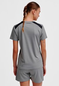 Szary sportowy top z krótkimi rękawami i czarnymi akcentami na ramionach, w zestawie z dopasowanymi szarymi szortami. Gładka, oddychająca tkanina o właściwościach odprowadzających wilgoć.