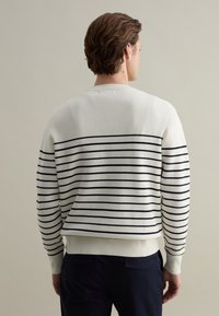 Striped sweater in cream with navy horizontal lines, featuring a crew neck and ribbed cuffs and hem, made from soft knit material.