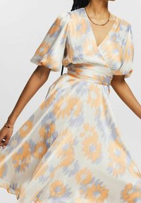 Robe à motif floral avec des manches courtes bouffantes, décolleté en V, taille cintrée et jupe fluide dans des tons pastel d'orange et de bleu sur fond blanc.