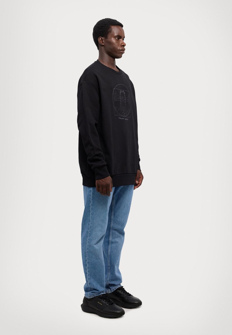 Sudadera negra con un logo texturizado en la parte frontal, combinada con unos vaqueros azul claro y zapatillas negras. La sudadera tiene un corte relajado.