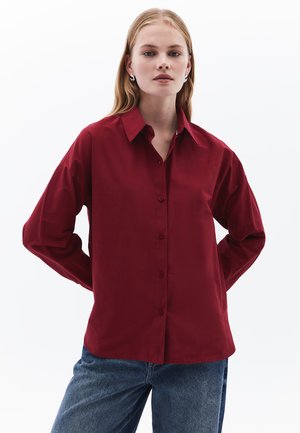 Rotes Langarmhemd mit Knopfleiste, klassischem Kragen und lockerer Passform, kombiniert mit Jeans. Glatte Textur.
