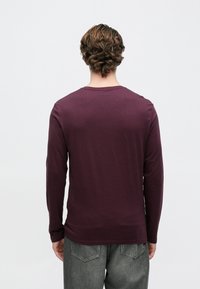 Pikaaegne särk tumepunases burgundi värvitoonis, ümara kaelusega, keha järgiva lõikega, sileda tekstuuriga, kombineeritud helehallide teksadega, tagant vaadatuna.