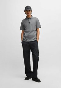 Grå polo shirt med krave og korte ærmer, parret med sorte cargo bukser med sidelommer. Sort kasket fuldender looket.