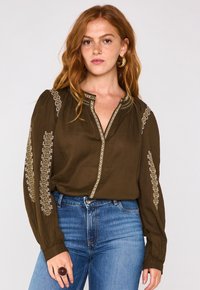 Blusa a maniche lunghe verde oliva con ricami dorati lungo le spalle e il pattino, caratterizzata da un collo a V poco profondo e maniche arricciate.