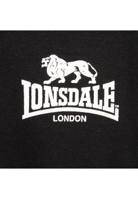 Svart textil med en stickad textur som har en vit leont logo ovanför ordet "LONSDALE" och "LONDON" nedanför i fet stil.