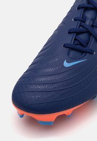Botín de fútbol Nike en azul oscuro, con una parte superior texturizada y con relieves, acentos naranjas en la suela y un logotipo azul claro.