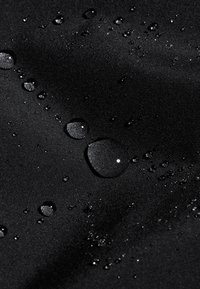 Gocce d'acqua che si accumulano su un tessuto nero liscio, evidenziando la sua texture resistente all'acqua e gli effetti della tensione superficiale.