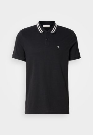 Mustust polo-särk, mis on valmistatud siledast puuvillast. Omab kaht nuppu särgi avamisel ja kontrastset triibulist kraed. Väike logo rinna piirkonnas.