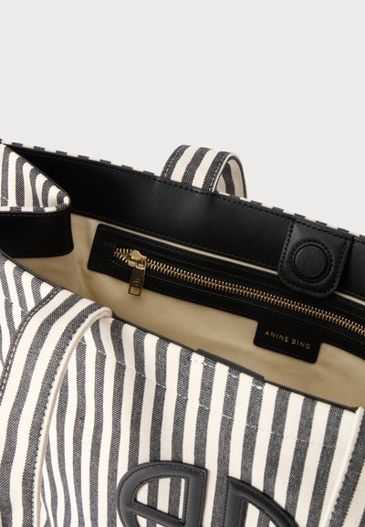 Sac cabas rayé noir et blanc avec garniture en cuir noir, poche zippée dorée à l'intérieur et étiquette de marque "Anine Bing" sur la doublure intérieure beige.