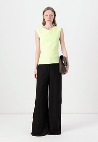 Ermeløs lysegrønn topp med teksturerte vertikale linjer, kombinert med løstsittende svarte cargo-bukser som har store sidelommer.