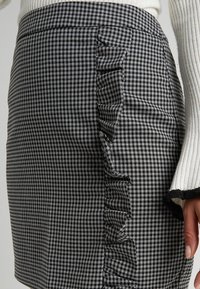 Black and white houndstooth skirt with vertical ruffle detail worn with a white ribbed sweater sleeve visible at side.